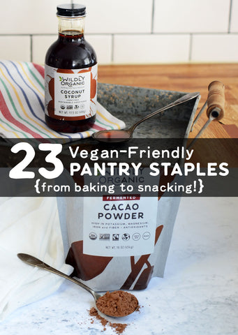 Coconut syrup bottle, cacao powder bag, and spoon with text 23 Vegan-Friendly PANTRY STAPLES from baking to snacking