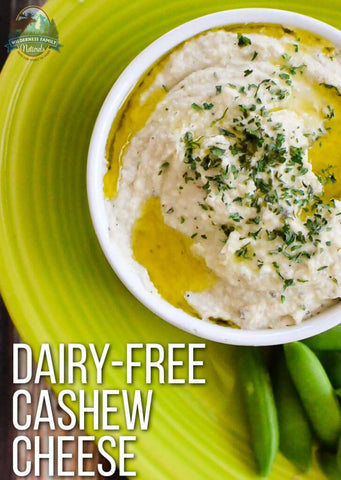 A bowl of dairy-free cashew cheese garnished with herbs on a green plate with snap peas